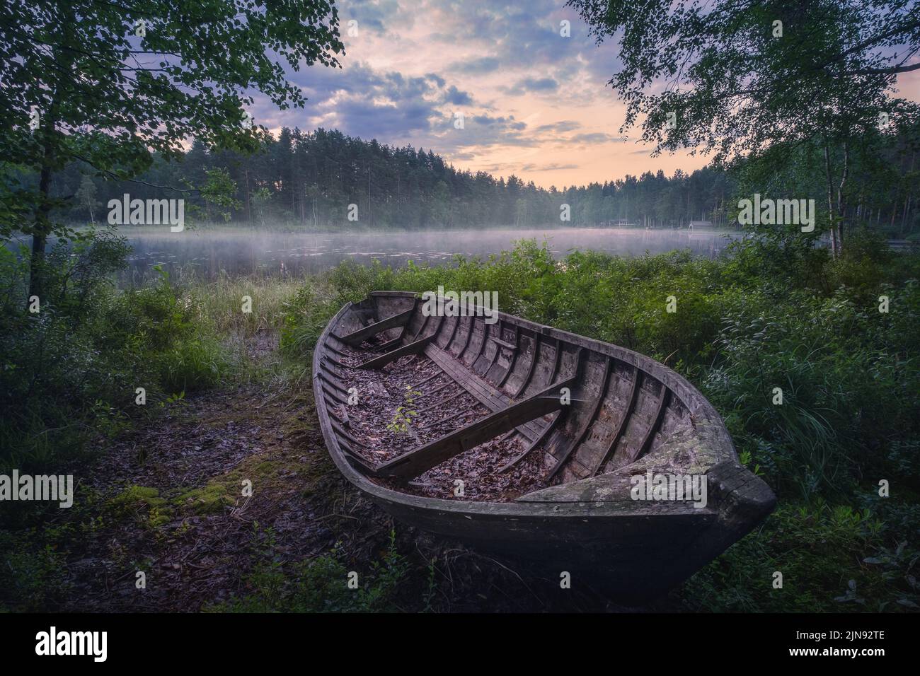Schöner Sonnenaufgang in einem ruhigen See am Sommerabend in Finnland mit einem Holzboot Stockfoto