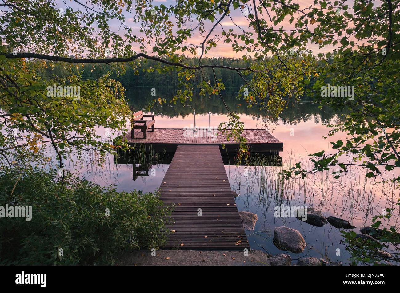 Schöner Sonnenuntergang in einem ruhigen See am Sommerabend in Finnland mit Pier Stockfoto