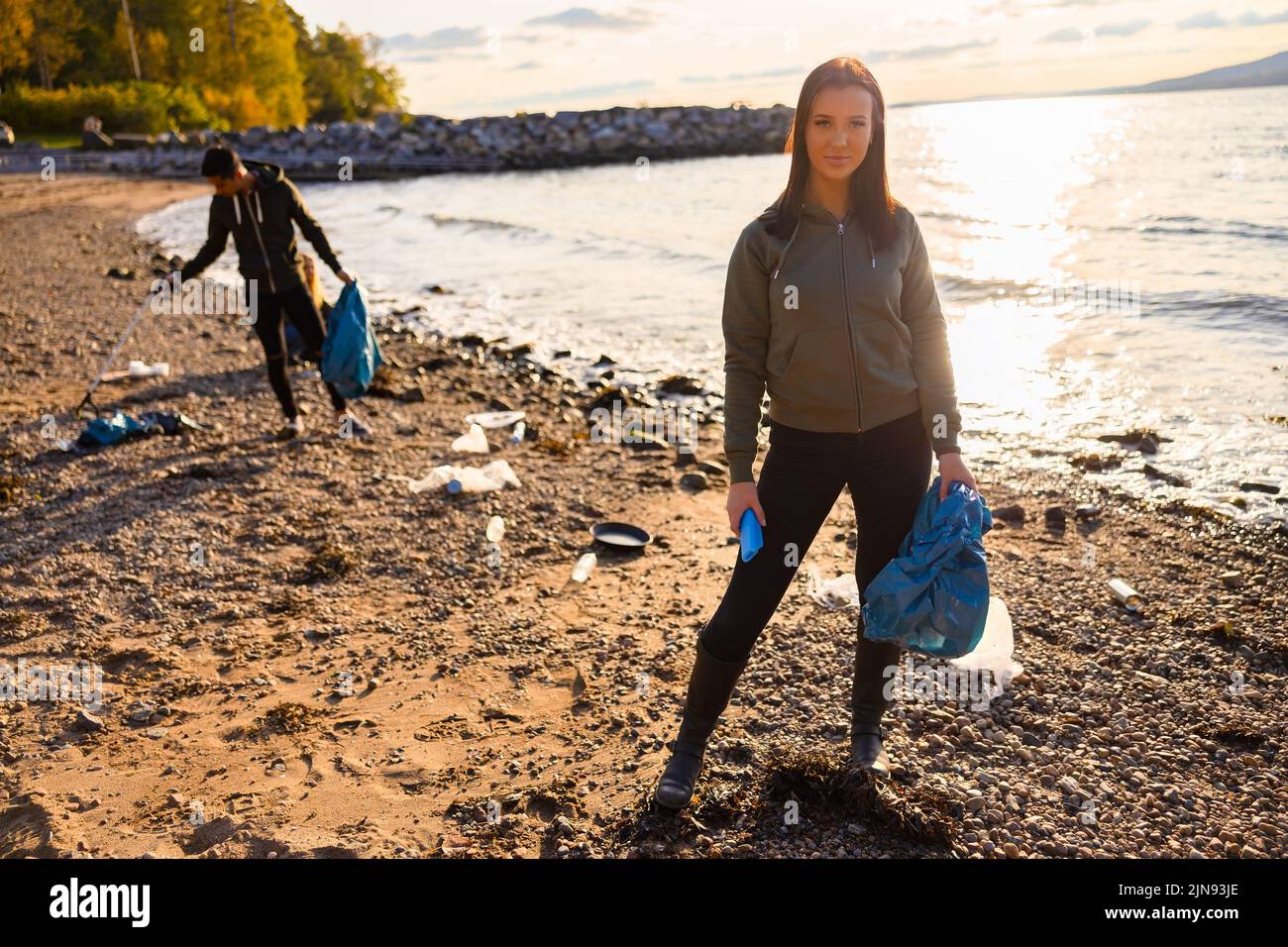 Serious junge Frau Reinigung Strand für Kunststoff mit Freiwilligen während schönen Sonnenuntergang Stockfoto