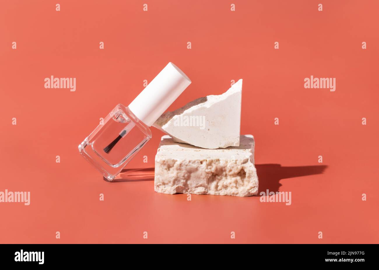Wiederfüllbare Flasche aus klarem Glas mit Bürstendeckel in der Nähe beigefarbener Travertin-Steine auf rosa, Nahaufnahme, Mockup. Hautpflege Nagel Produkt. Naturkosmetik, minimal Stockfoto