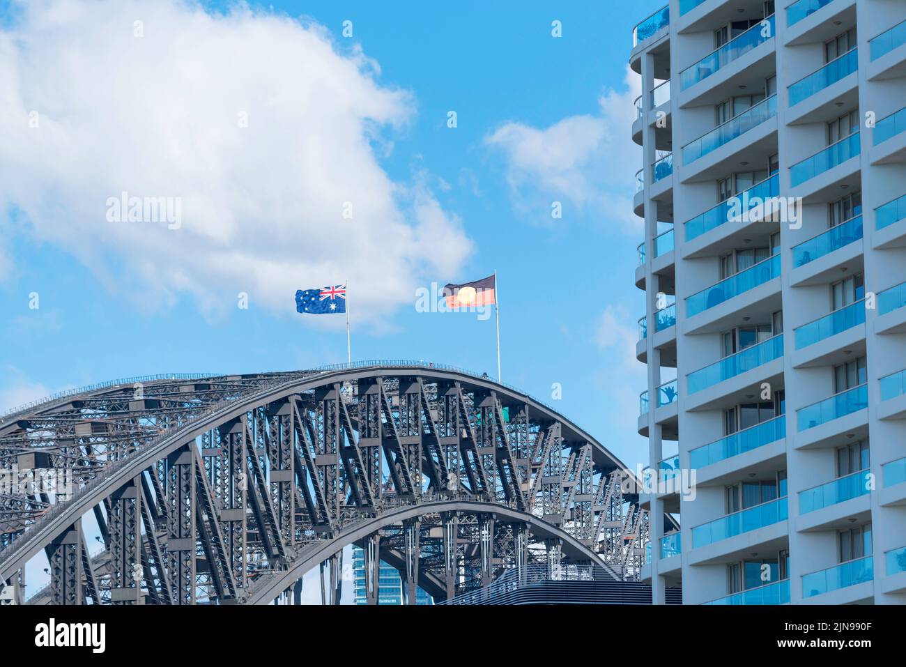 Von Kirribilli aus gesehen, fliegt die Flagge der Aborigines mit starkem Westwind nun neben der australischen Flagge über der Sydney Harbour Bridge Stockfoto
