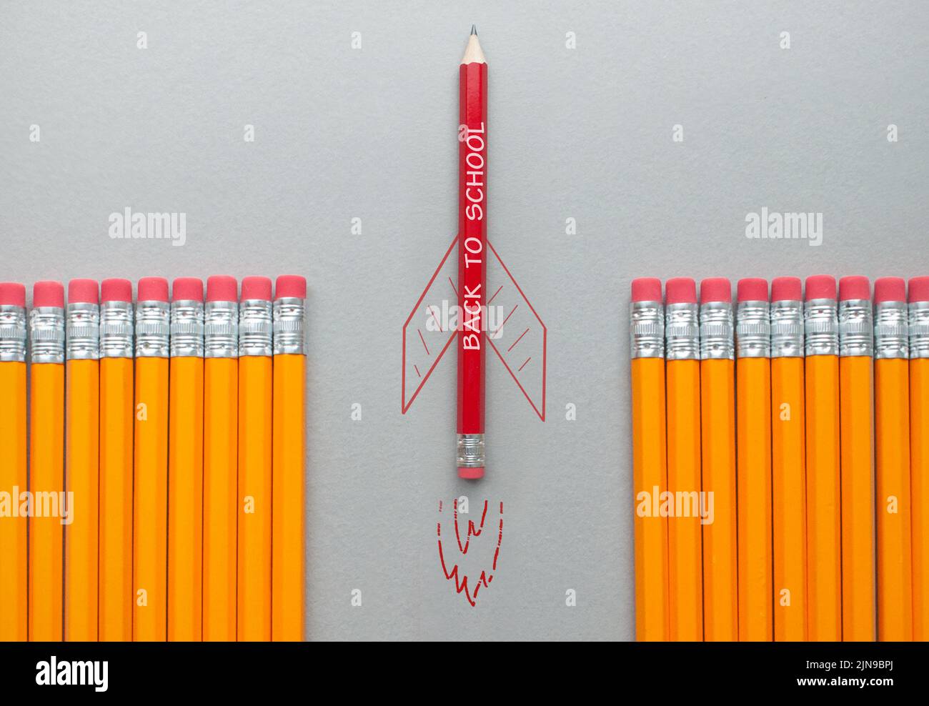 Zurück zur Schule roter Bleistift mit Raketenskizze, der sich zwischen einer Reihe orangefarbener Bleistifte heraussticht Stockfoto