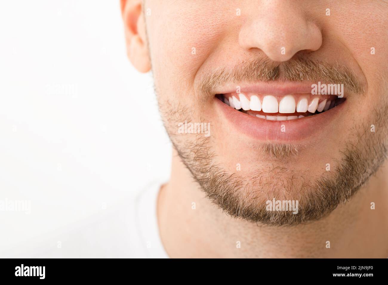 Ein schöner Mann lächelt. Ein Lächeln mit weißen Zähnen. Nahaufnahme des Bildes. Weißer Hintergrund mit Copyspace. Stockfoto