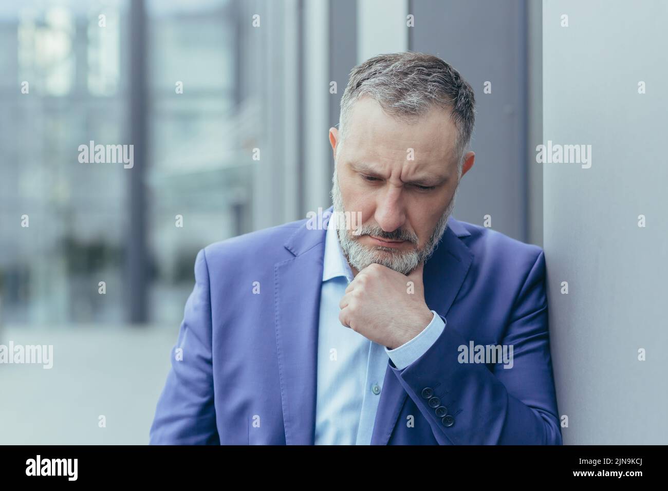 Leitender grauhaariger Mann vor dem Bürogebäude, stehend und denkend, verwirrt und traurig Geschäftsmann Chef in Business Anzug, über Entscheidung Stockfoto