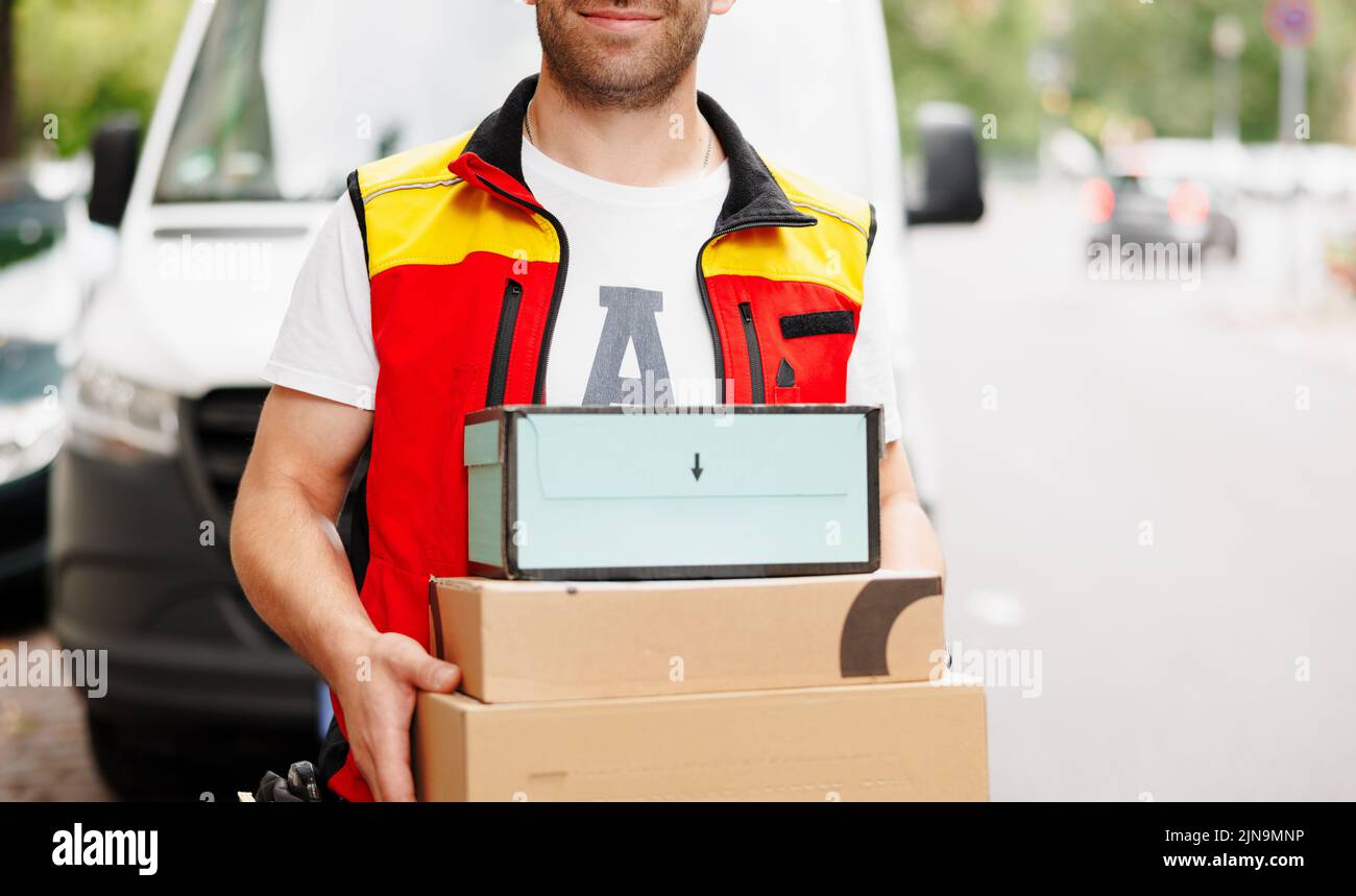 Der Lieferer hält Stapel von Kartons vor sich. Stockfoto