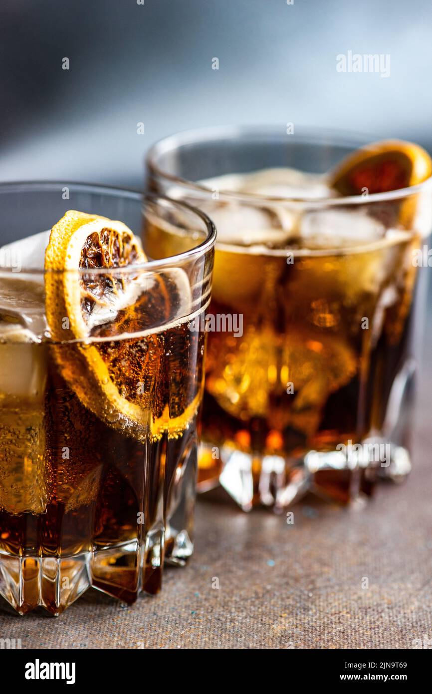 Alkoholcocktail mit Cola im Glas mit Orangenscheibe und Eiswürfeln auf dunklem Betontisch Stockfoto