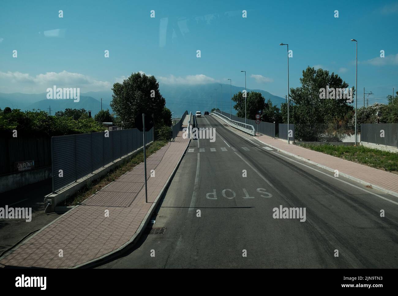 Eine Straße in Süditalien mit Stoppschild, Zebraüberquerung und Überführungsbrücke mit Bergen im Hintergrund. In der Nähe von Pompeji Italien. Stockfoto