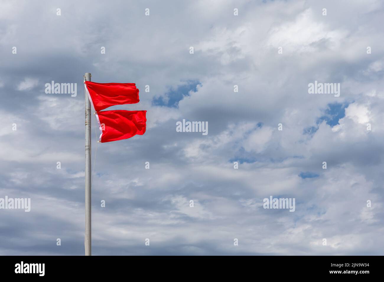 Doppelte rote Flaggen vor einem dramatisch bewölkten Himmel zeigen an, dass der Strand wegen gefährlicher Bedingungen zum Schwimmen gesperrt ist. Stockfoto