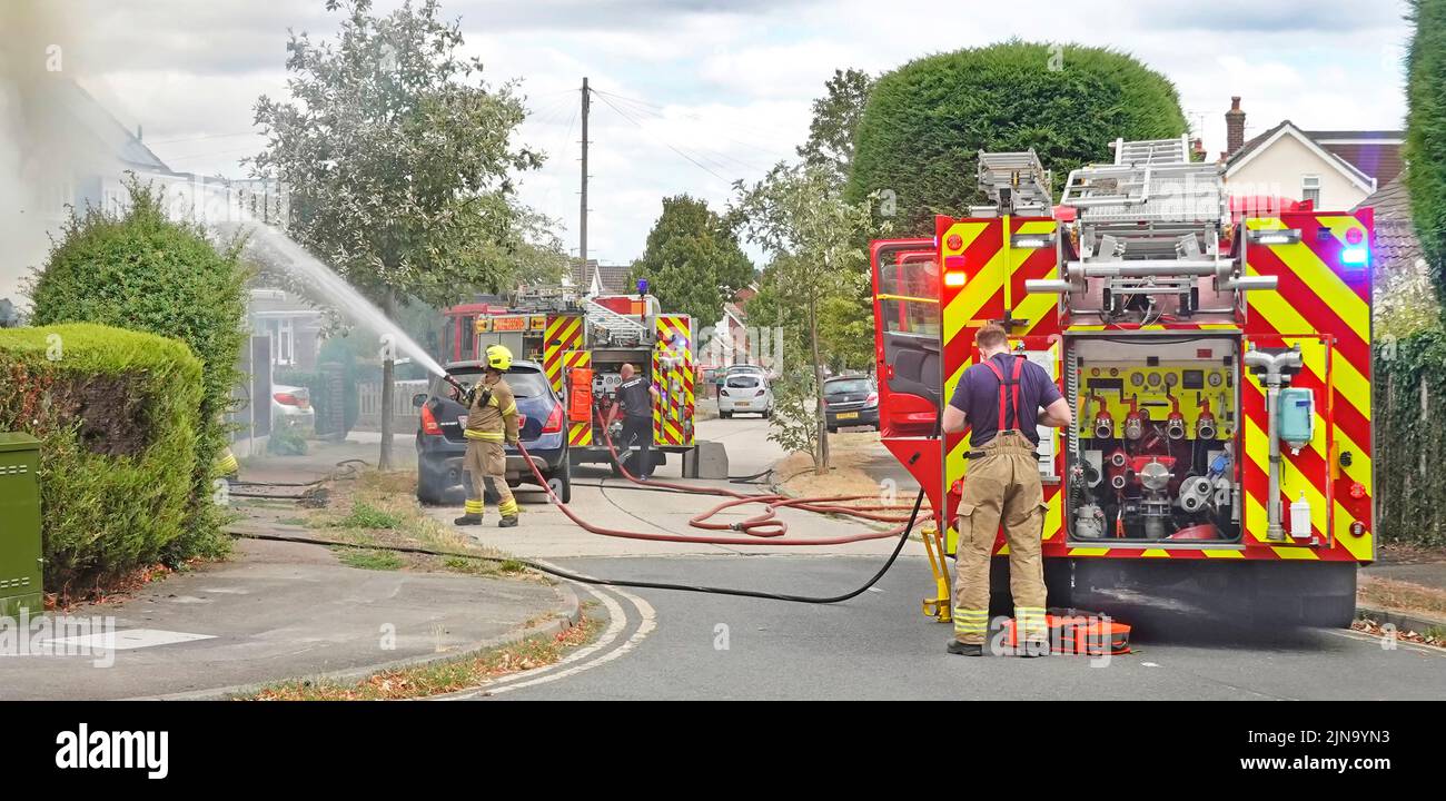 Feuerwehrmänner von Essex Fire and Rescue Service sprühen Wasserstrahl auf Haus zwei Feuerwehrfahrzeuge und Feuerwehrleute in Wohnstraßenlandschaft England Großbritannien Stockfoto