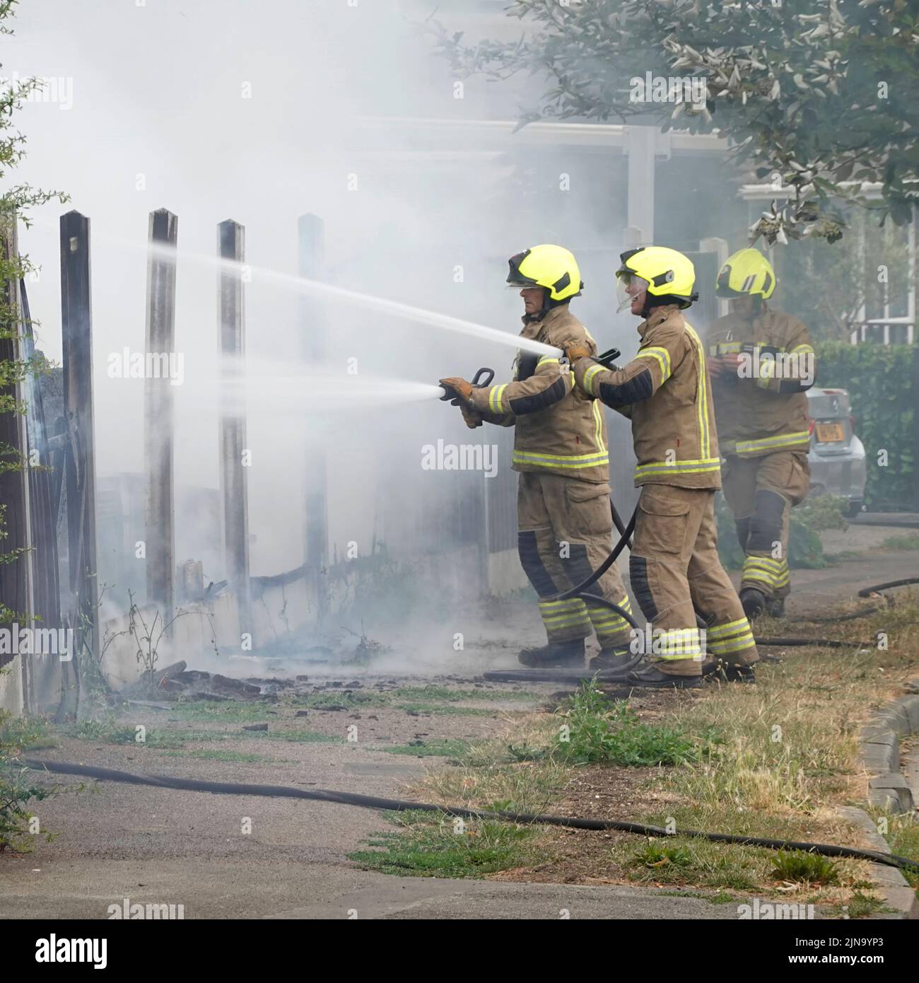 Essex Fire and Rescue Service Gruppe von Feuerwehrleuten in Schutzkleidung gefährliche und gefährliche Arbeitshausbrand mit Wasserschläuchen England Großbritannien Stockfoto