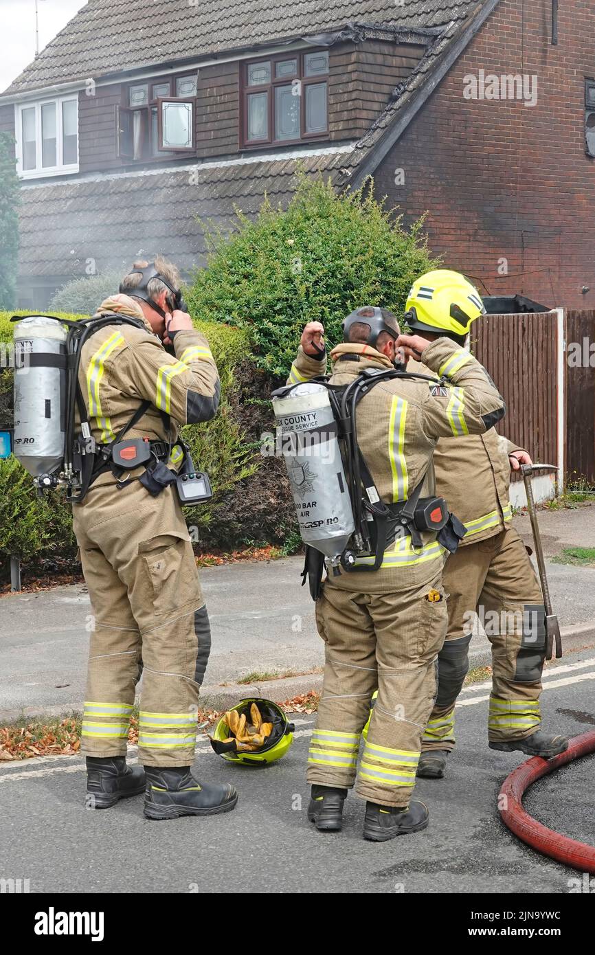 Ausrüstung und Helme von Atemschutzgeräten werden bei Feuerwehrleuten der britischen Feuerwehr in Schutzkleidung beim Hausbrand in England montiert Stockfoto