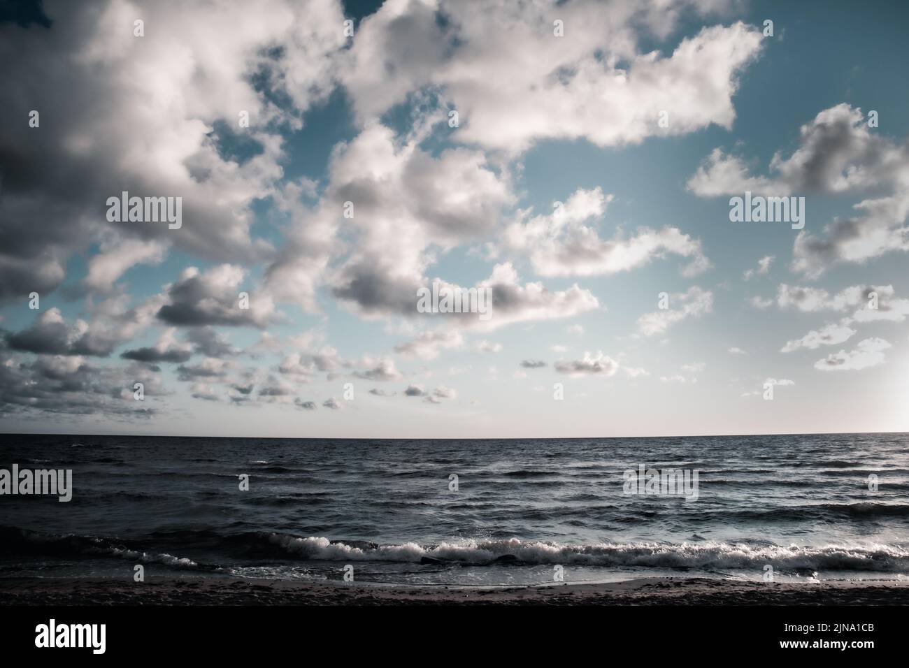 Wolkiger Tag am Strand mit kühlen Farben. Weiße, graue, schattige Wolken und welliges Meer. Kontrast. Stockfoto