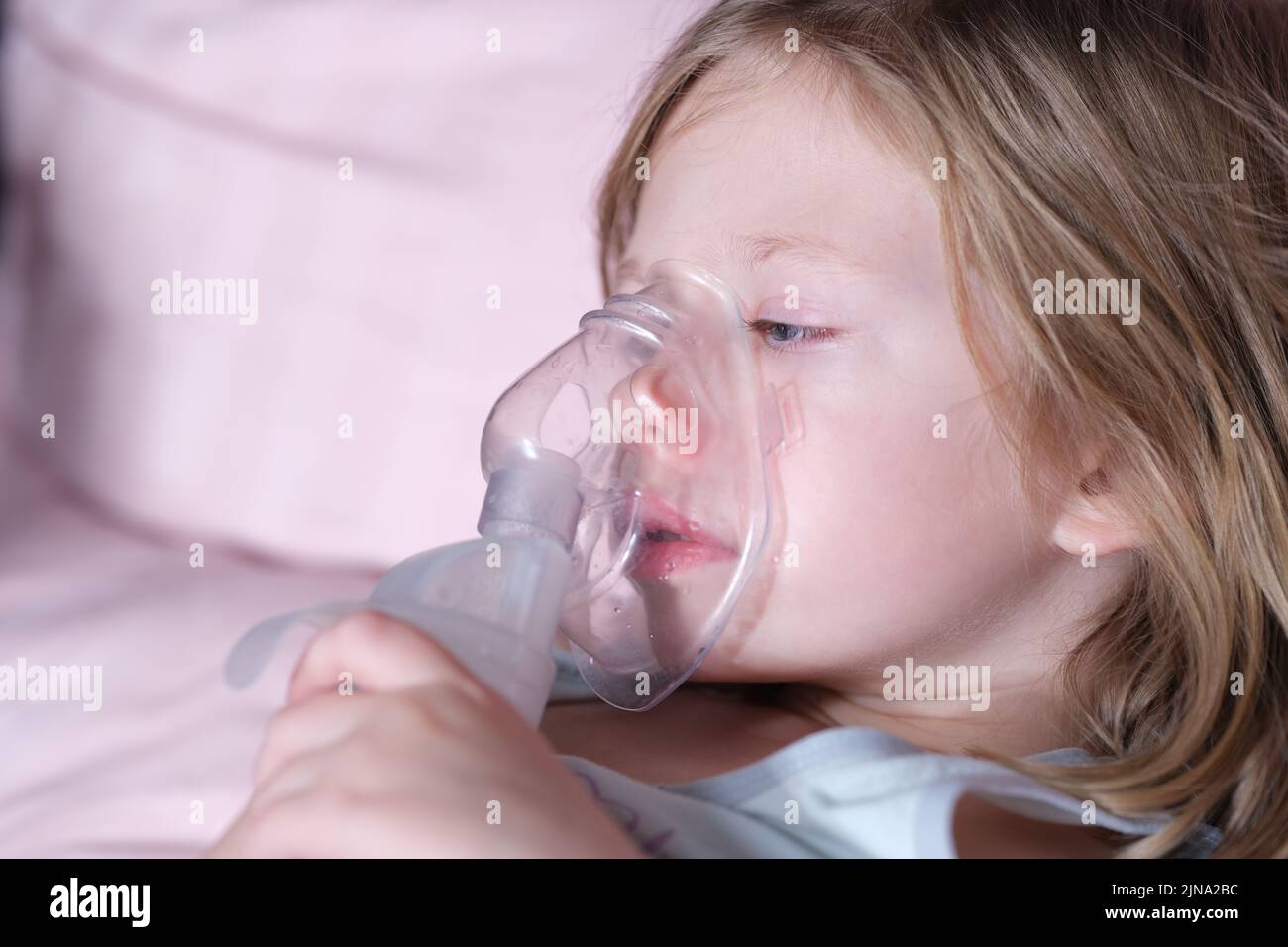 Krankes Mädchen in Sauerstoffmaske liegt auf Krankenhausbett Stockfoto