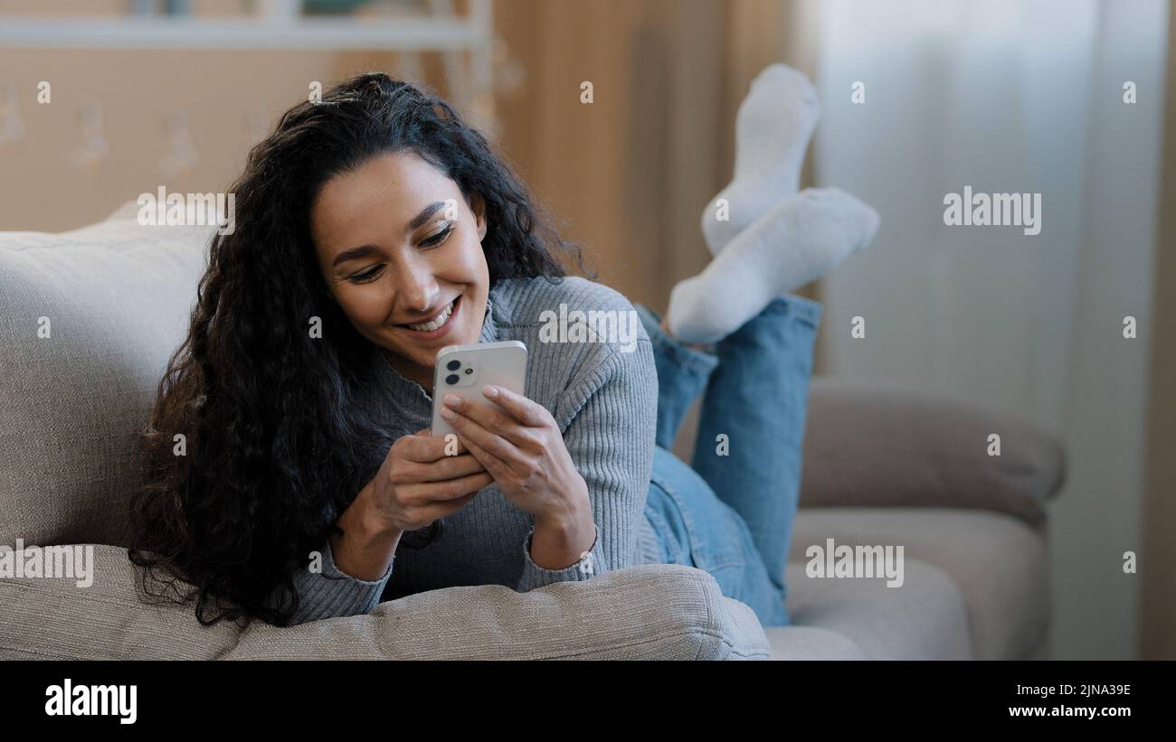 Attraktive 25s Mädchen liegen auf der Couch halten Telefon ruhen entspannen Spaß im Internet chatten junge Frau lächelnd genießen Wochenende online machen Stockfoto