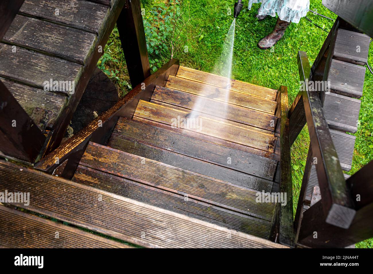 Nahaufnahme der Verwendung eines Hochdruckreinigers zur Reinigung von imprägnierten Holzterrassentreppen im Freien im Frühjahr. Vor und nach der Reinigung, großer Kontrast. Stockfoto