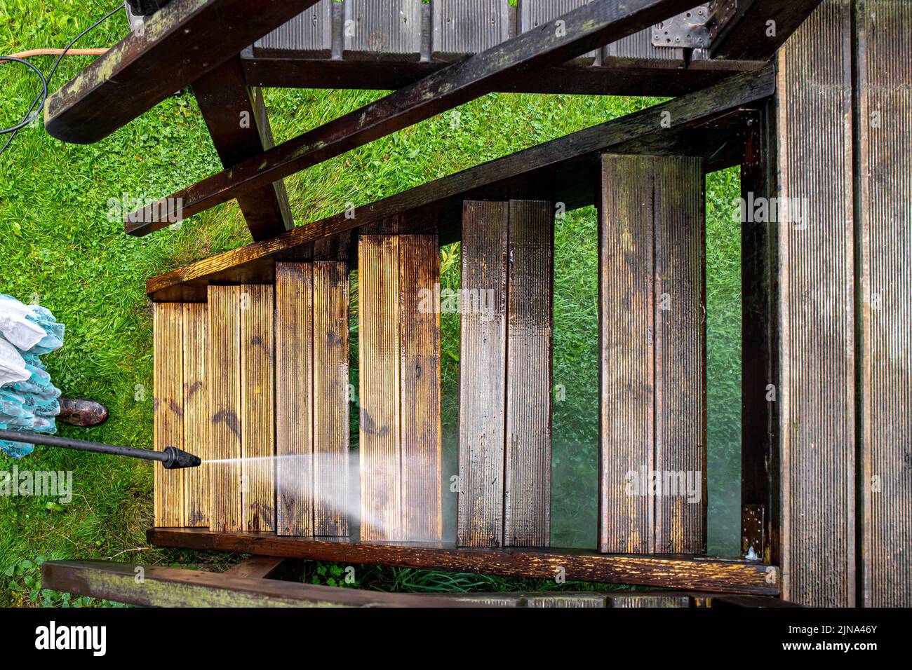Nahaufnahme der Verwendung eines Hochdruckreinigers zur Reinigung von imprägnierten Holzterrassentreppen im Freien im Frühjahr. Vor und nach der Reinigung, großer Kontrast. Stockfoto