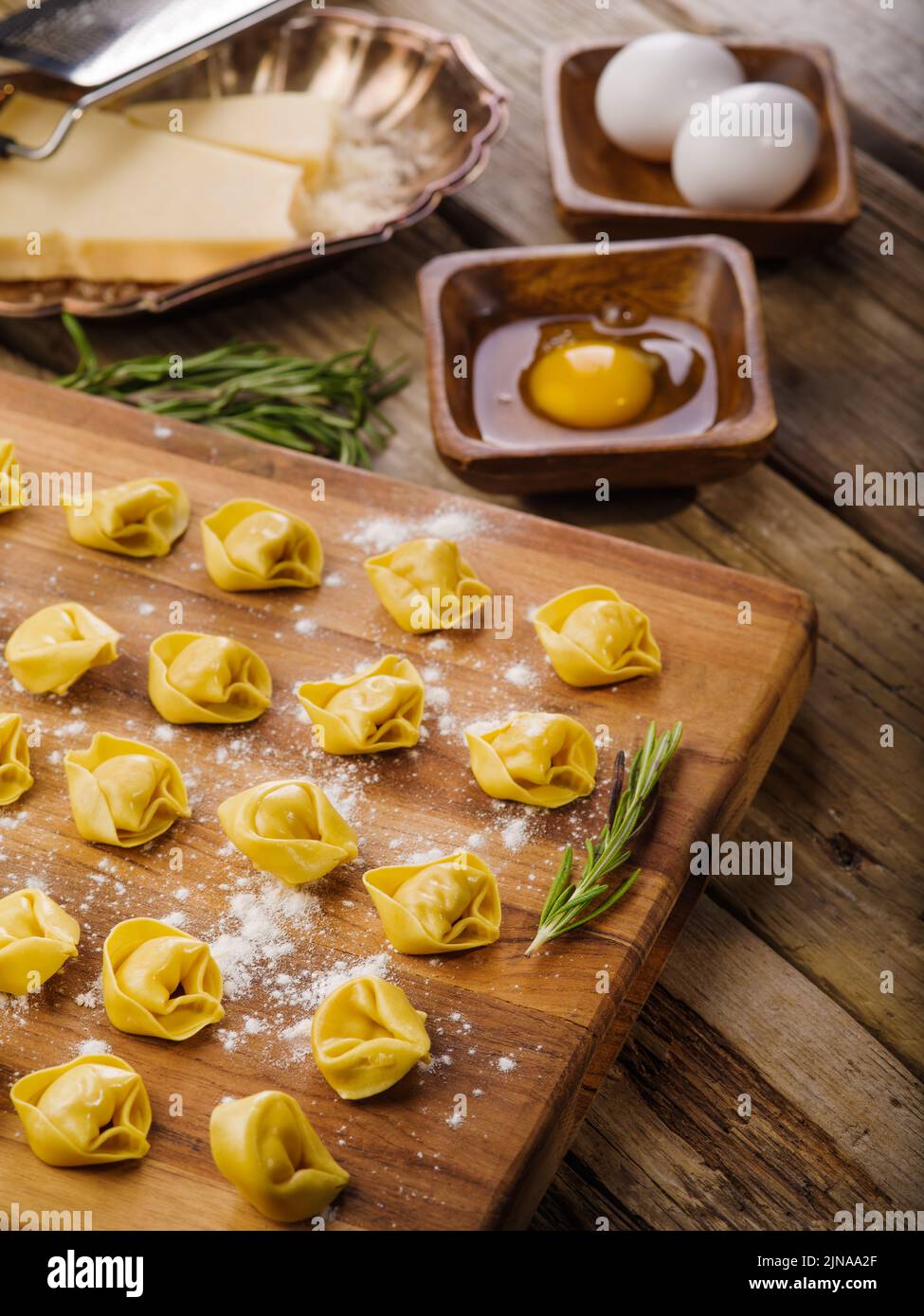 Auf einem hölzernen Schneidebrett befinden sich kleine hausgemachte Ravioli, gefüllt mit Hackfleisch, duftenden Rosmarinzweigen, Kochzutaten. Home Rezepte, Familie tra Stockfoto
