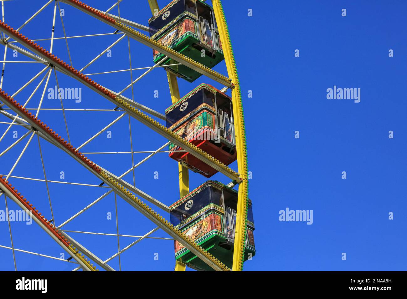 Riesenrad, Kapseln oder Kutschen auf farbenfroher Kirmes-Fahrt gegen den klaren blauen Himmel Stockfoto