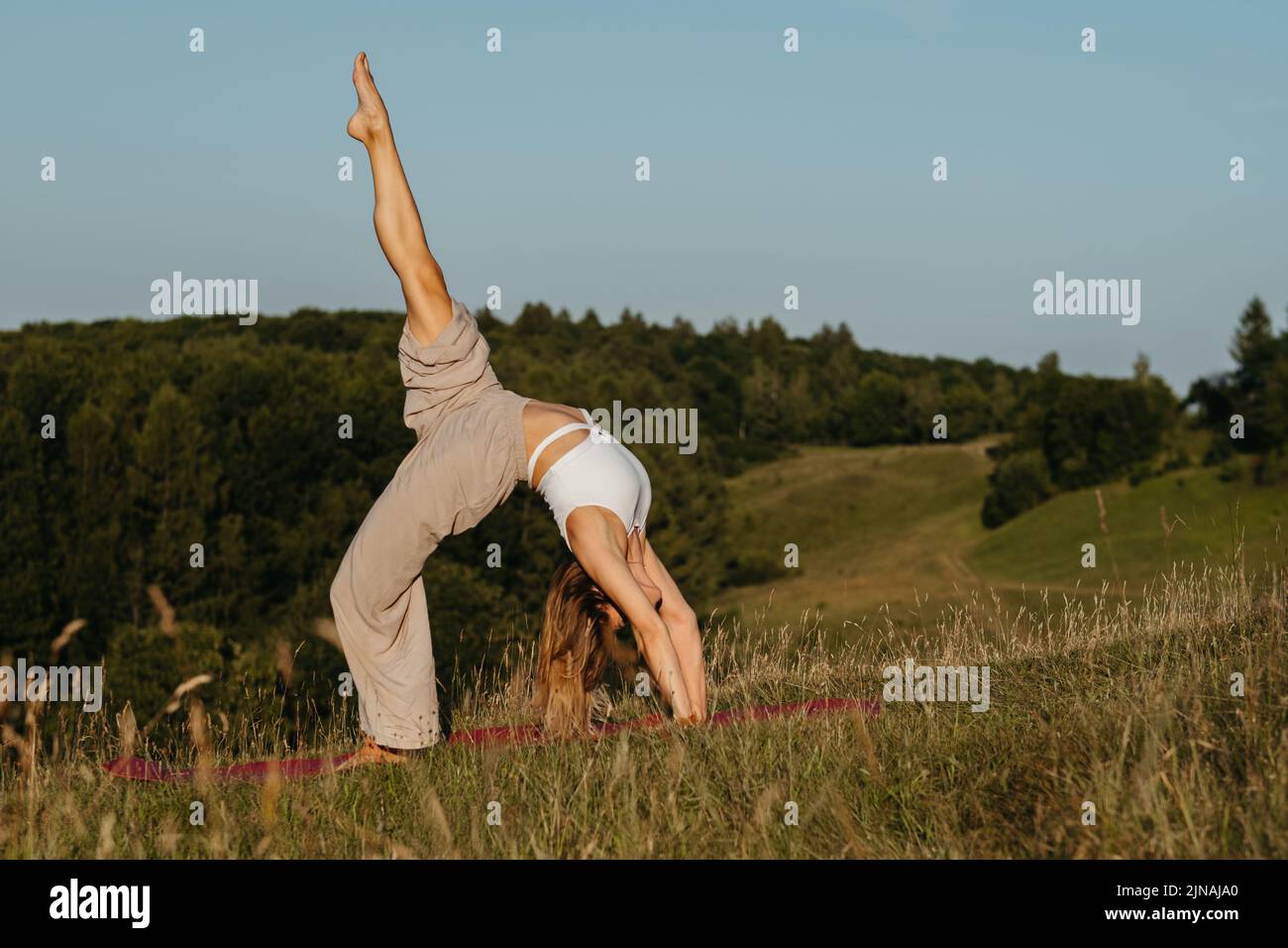 Junge Frau praktiziert Yoga im Freien mit blauem Himmel auf dem Hintergrund und landschaftlicher Landschaft bei Sonnenuntergang Stockfoto