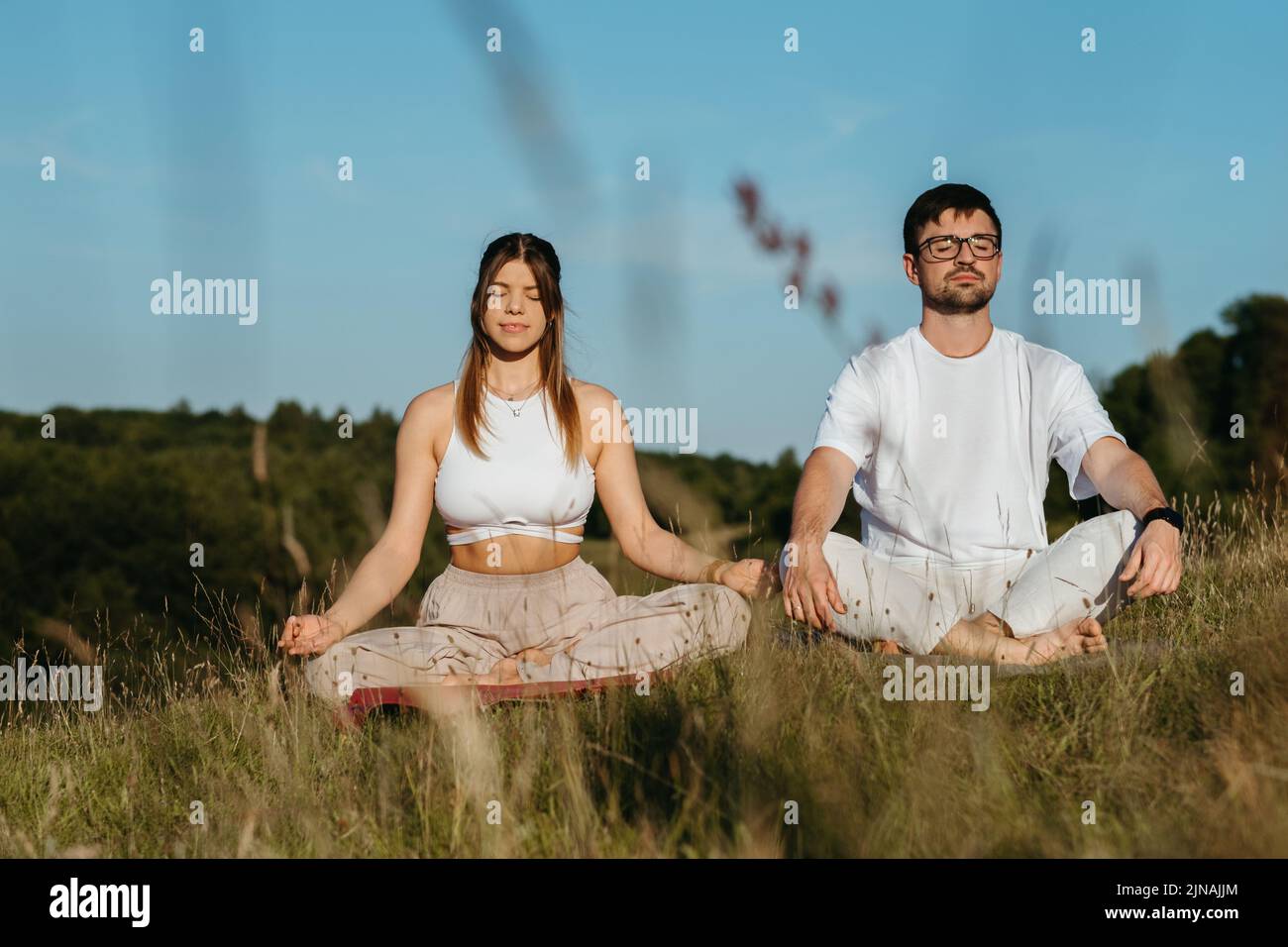 Junge Erwachsene Paare meditieren im Freien, kaukasische Frau und Mann kleideten sich gleichermaßen und atmen frische Luft in der Natur Stockfoto