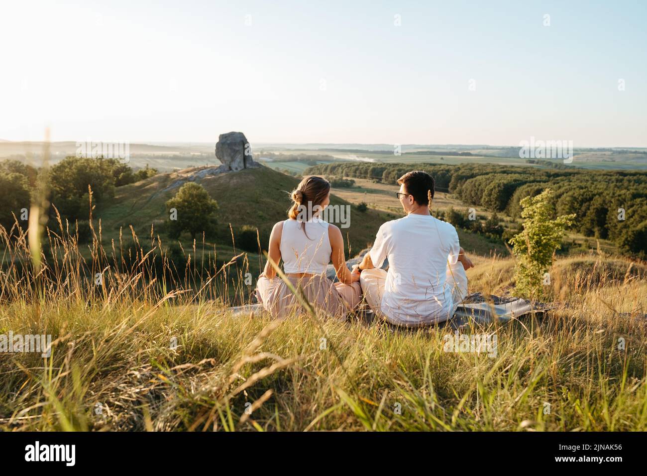 Mann und Frau üben Yoga und Meditation im Freien bei Sonnenuntergang mit szenischer Landschaft und Naturwunder Riesenstein auf dem Hintergrund Stockfoto