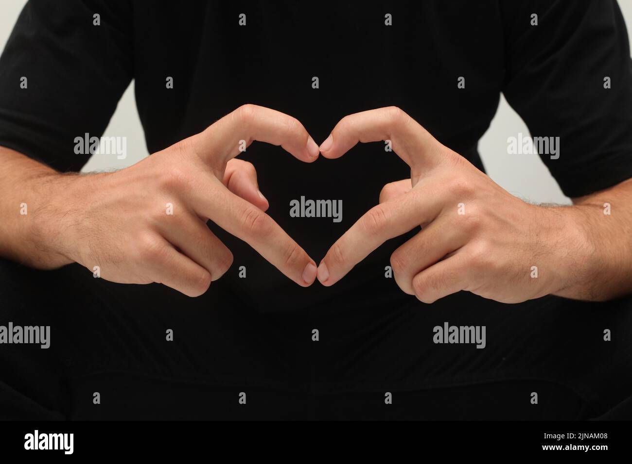 Die Hände des Mannes zeigen das Herzsymbol, isoliert auf Schwarz. Ein Mann in Schwarz, der mit den Fingern ein Herzsymbol zeigt. Liebesgestenkonzept. Stockfoto