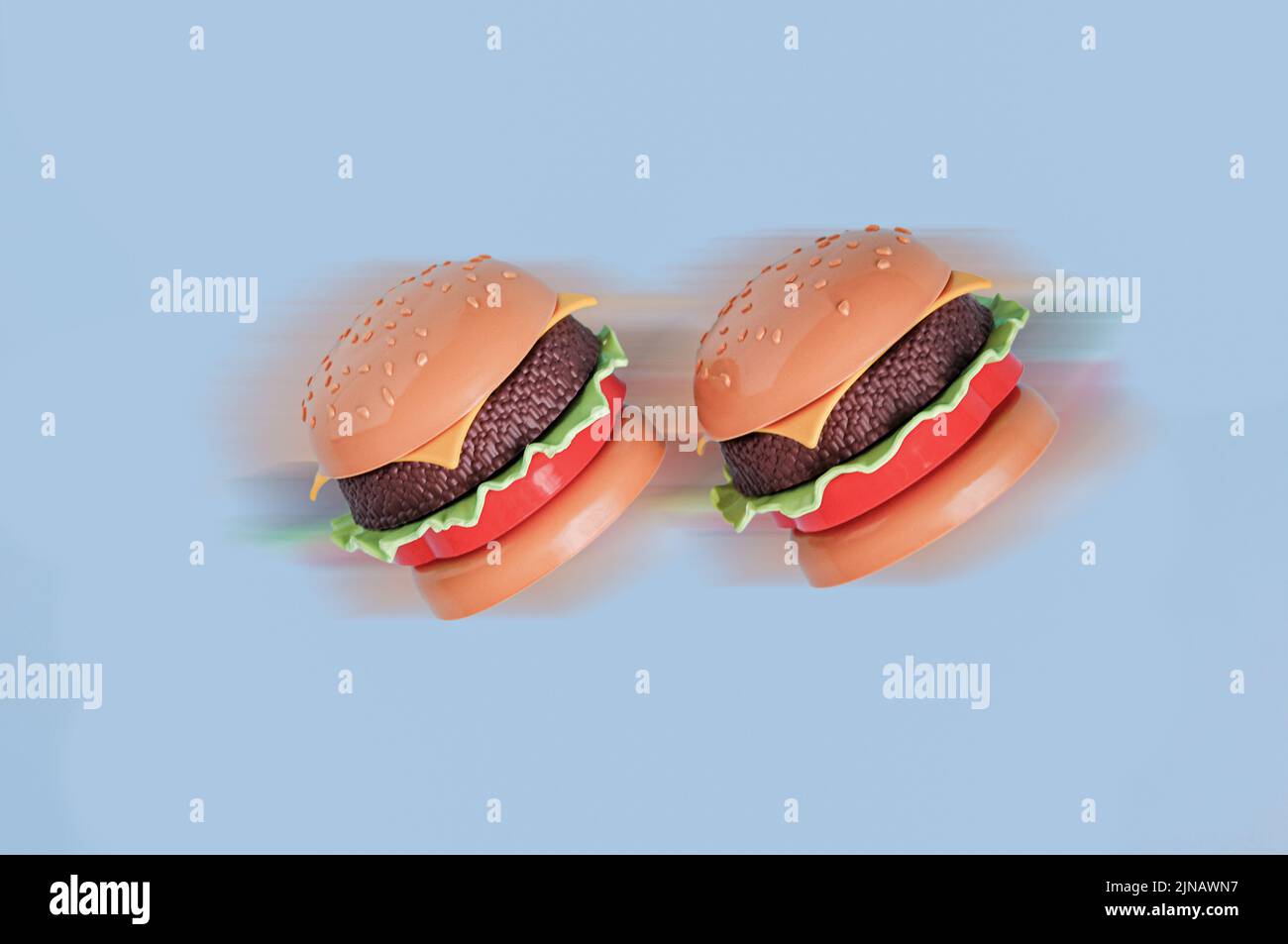 Plastikspielzeug-Burger für Kinder mit Salat, Tomaten, Fleisch auf Blau. Konzept der schnellen Lieferung. Menübestellung, Lebensmittelindustrie Stockfoto