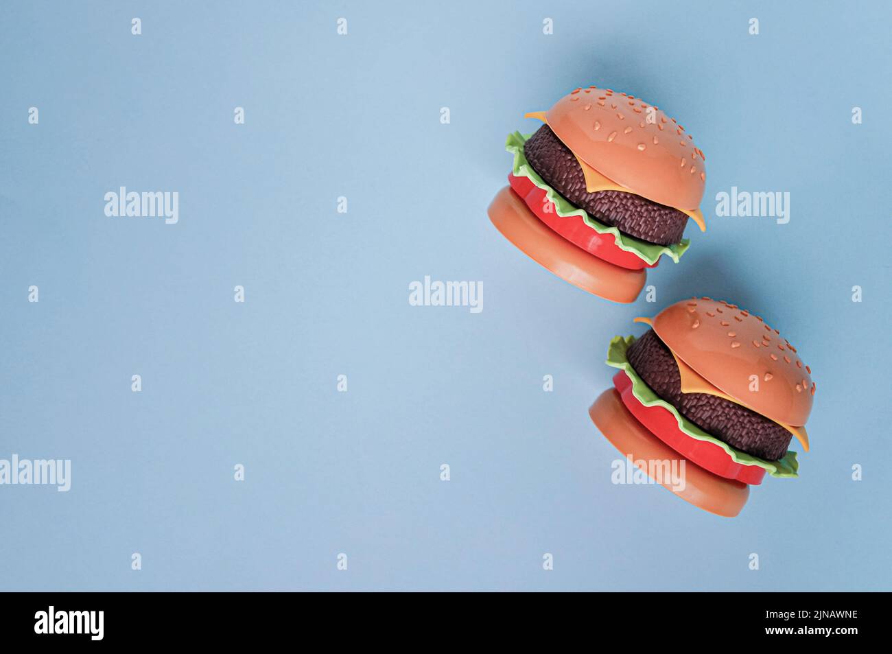 Plastikspielzeug-Burger für Kinder mit Salat, Tomaten, Fleisch auf Blau. Konzept der schädlichen künstlichen Nahrung. Ungesund. Nicht organisch. Nicht nützlich. Wir untersuchen heute Stockfoto