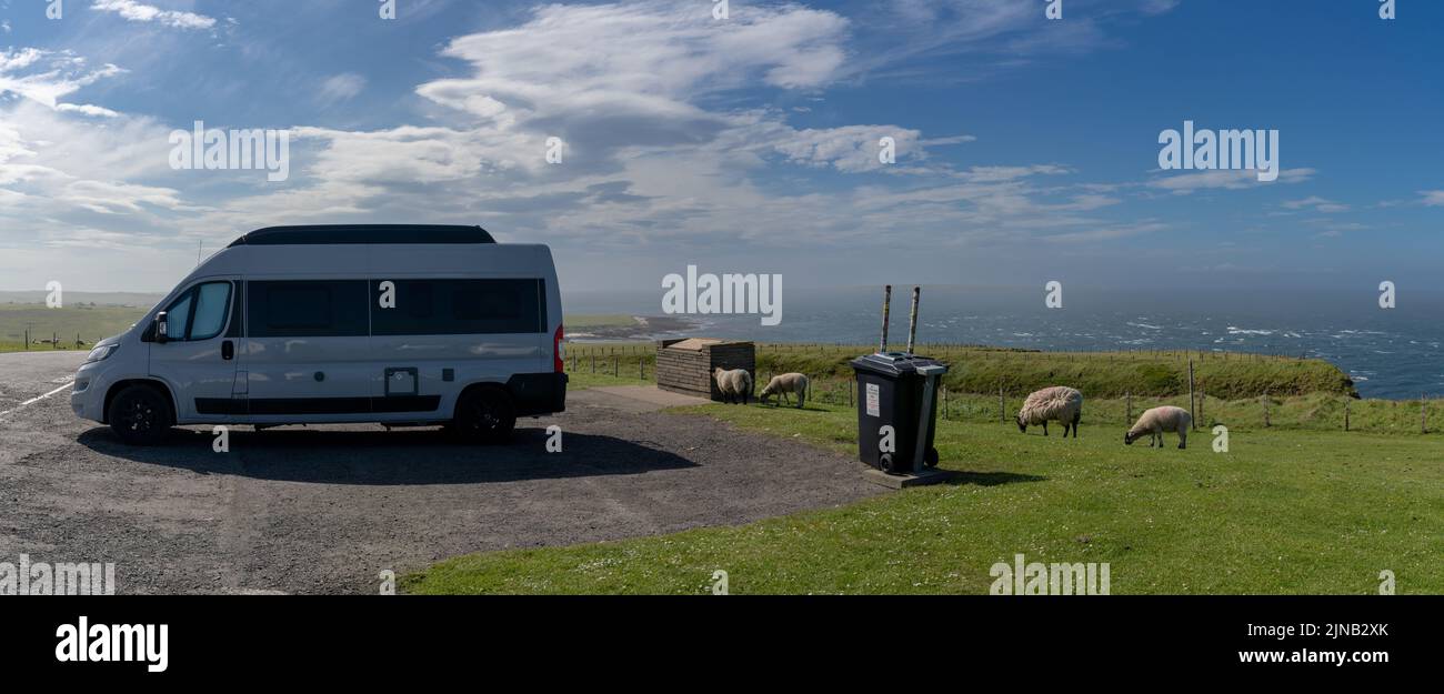 Eine Panoramalandschaft von John O'Groats und ein grauer Wohnmobil mit weißen Schafen im Vordergrund Stockfoto