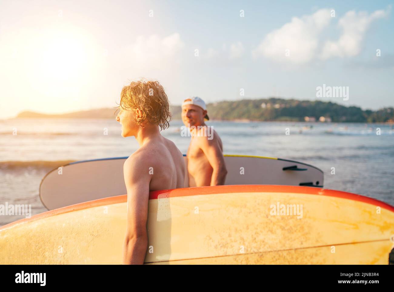 Teen boy mit Surfbrett gehen zum Meer zum Surfen mit Vater auf Sri Lanka Insel. Sie haben einen Winterurlaub und genießen einen schönen Sonnenuntergang Licht F Stockfoto