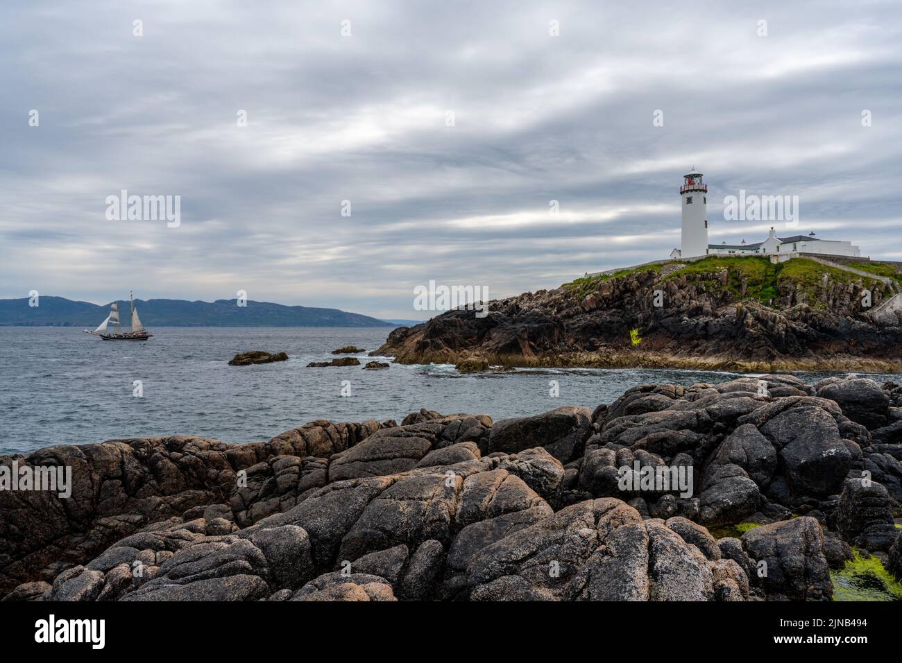 Ein Blick auf den Fanad Head Lighthouse an der Nordküste Irlands mit einem alten zweimastigen Segelboot, das absegelt Stockfoto