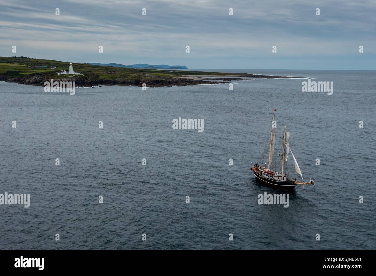 Ein Blick auf den Fanad Head Lighthouse an der Nordküste Irlands mit einem alten zweimastigen Segelboot, das absegelt Stockfoto