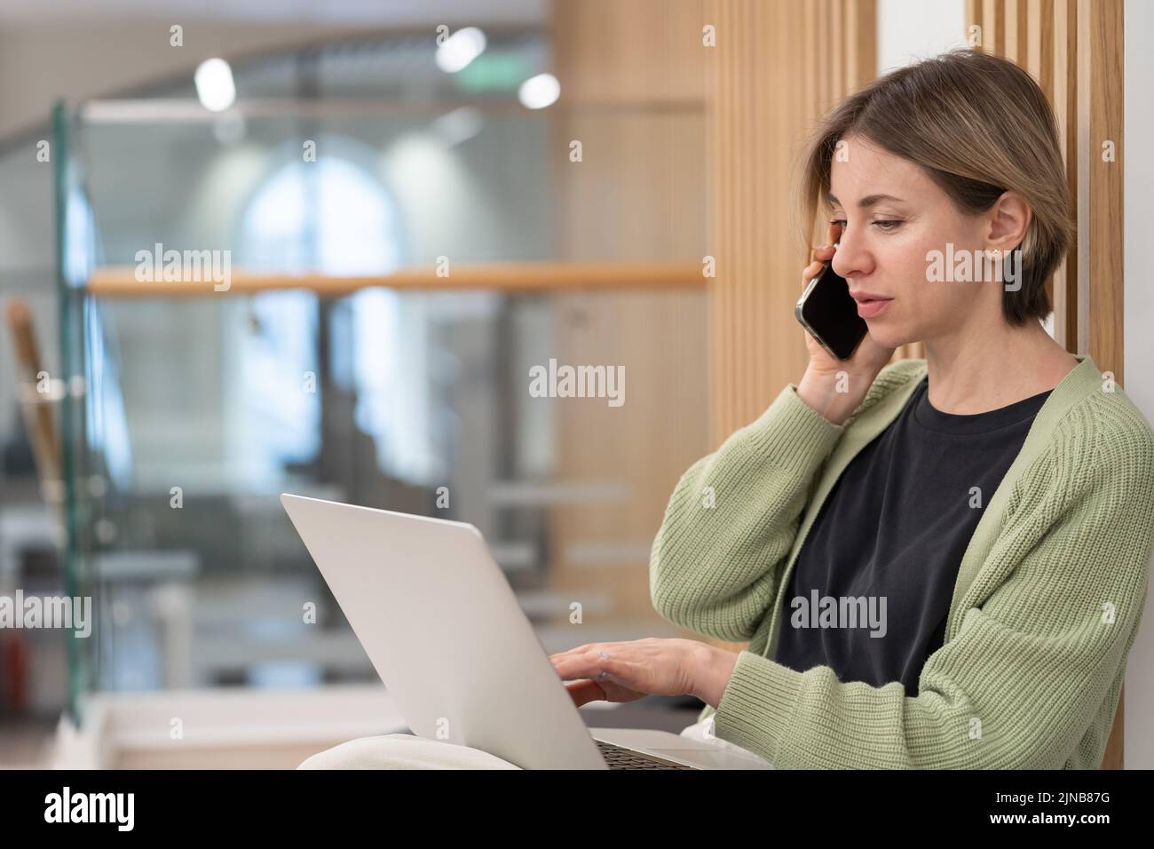 Seriöse Geschäftsfrau diskutiert über Projektdetails per Handy, während sie ferngesteuert am Laptop arbeitet Stockfoto