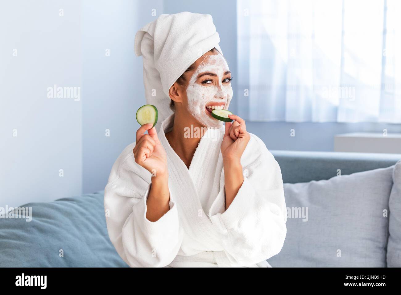 Schöne junge Frau mit Gesichtsmaske auf dem Gesicht, die Scheiben frischer Gurken hält. Hautpflege und -Behandlung, Spa, natürliche Schönheit und Kosmetologie Konz Stockfoto