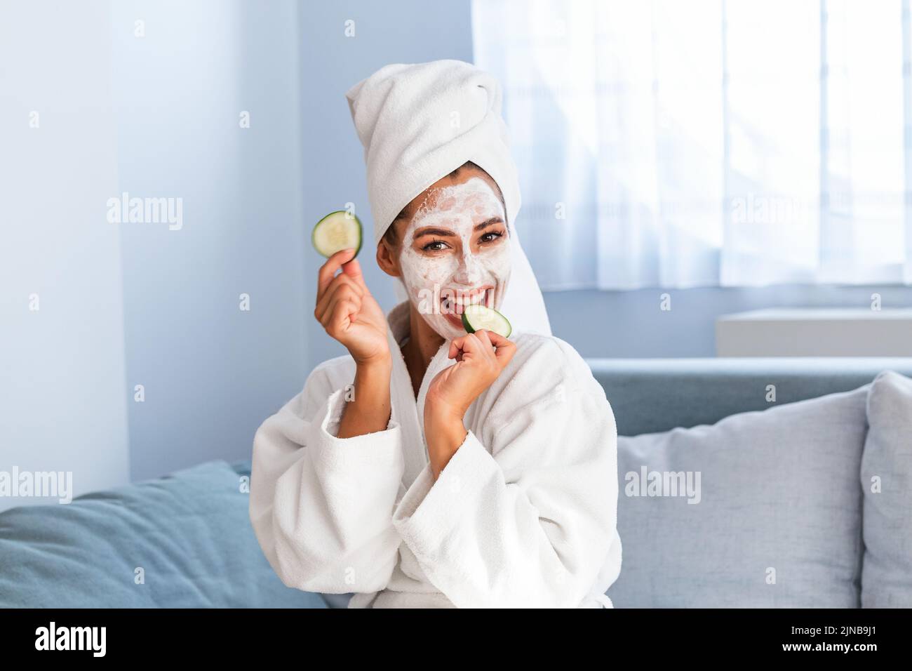 Schöne junge Frau mit Gesichtsmaske auf dem Gesicht, die Scheiben frischer Gurken hält. Hautpflege und -Behandlung, Spa, natürliche Schönheit und Kosmetologie Konz Stockfoto