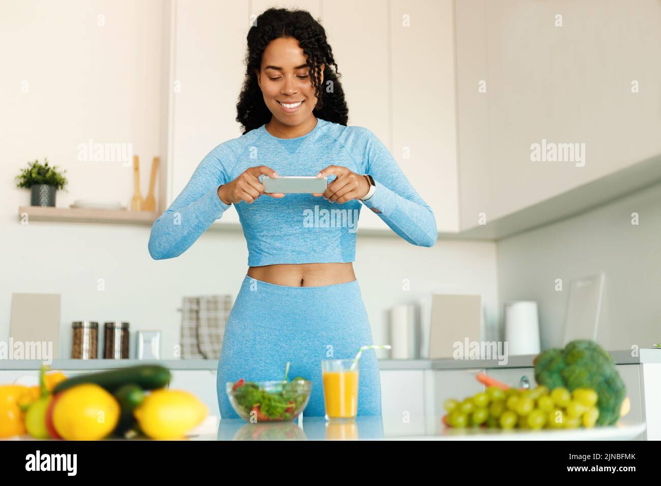 Food and Fitness Blogging Konzept. Fit schwarze Dame Foto von gesunden Abendessen auf dem Smartphone, stehend in der Küche Stockfoto