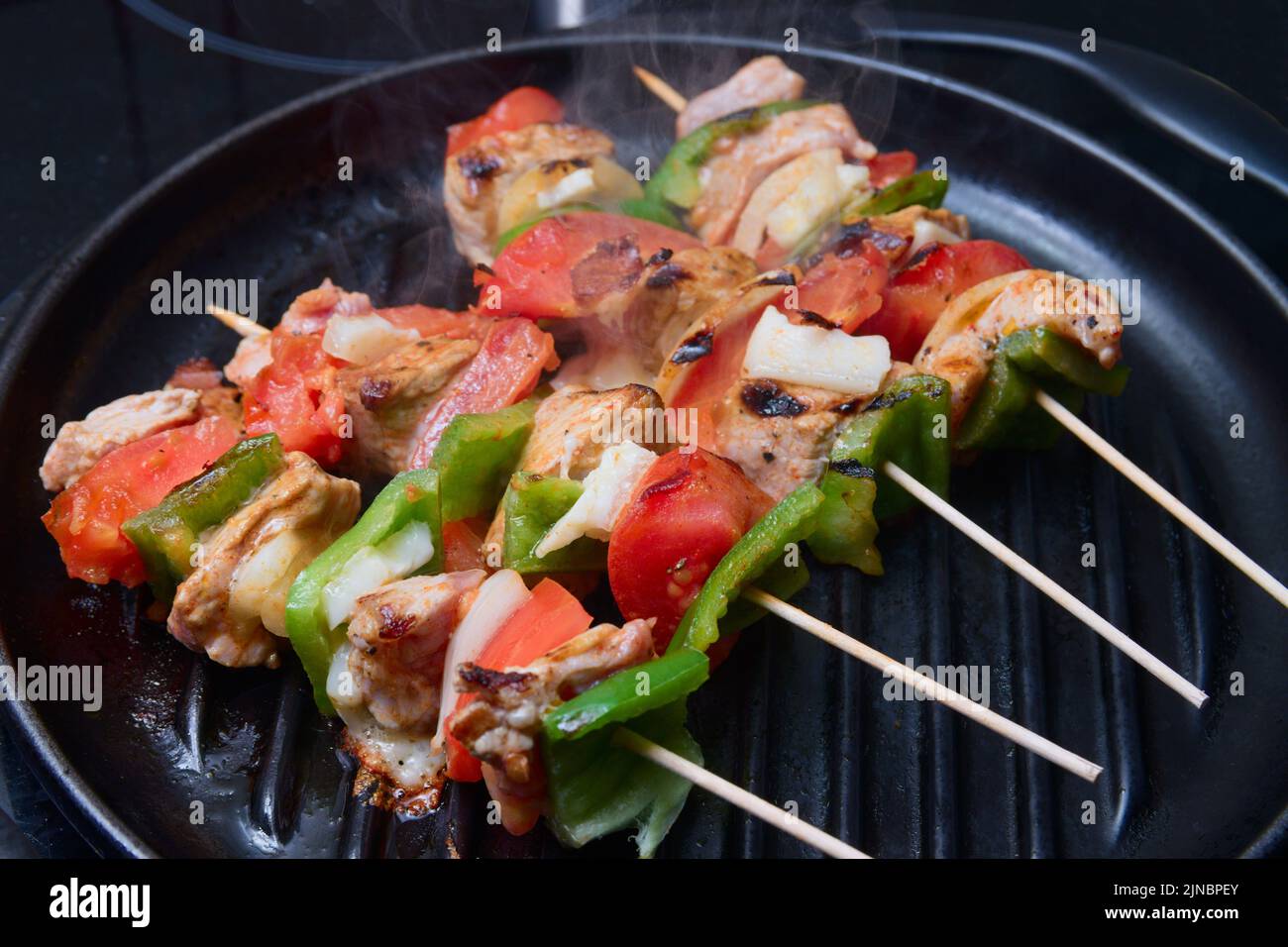 Leckere hausgemachte Fleisch- und Gemüsespieße, die auf einem schwarzen Grill gegrillt werden Stockfoto