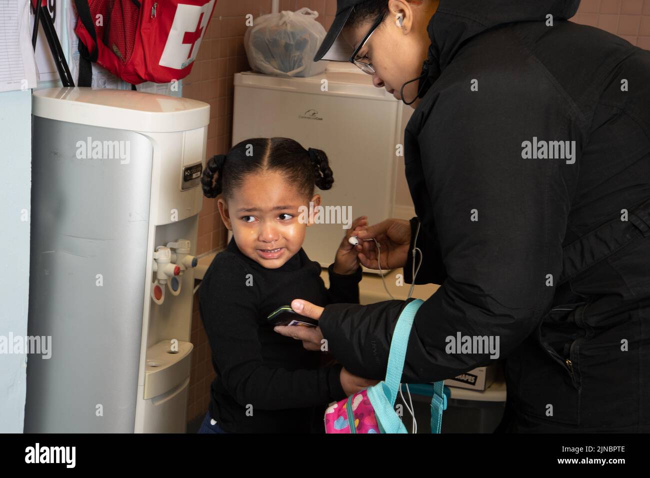 Bildung Vorschule Kinderbetreuung Beginn des Tages Trennung Mädchen weinend in Erwartung der Trennung Mutter lehnte sich hin, um ihr etwas am Telefon zu zeigen Stockfoto