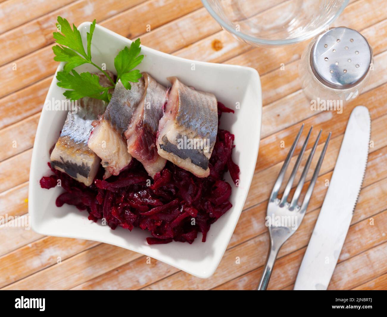 Leicht gesalzene Heringsscheiben mit geriebenen Rüben und Grünpflanzen Stockfoto