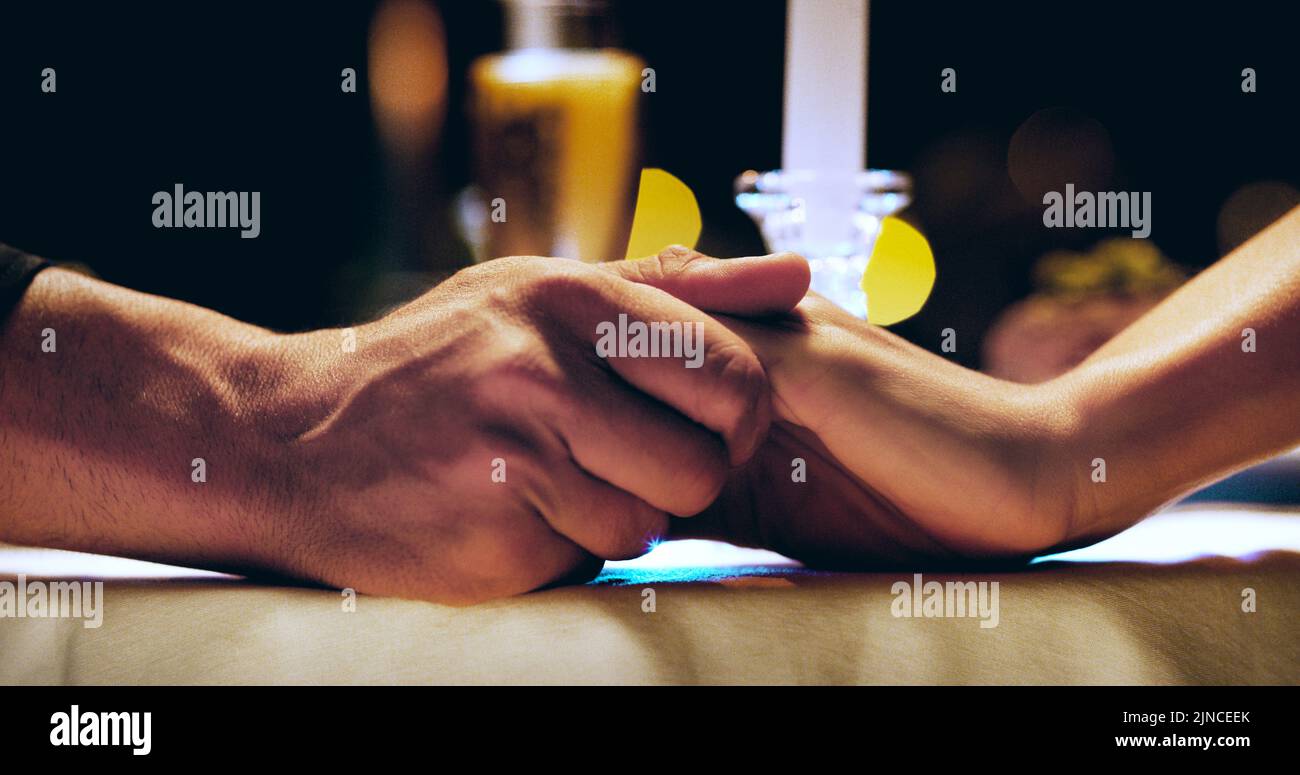 Hand in Hand zusammen, für immer. Ein unerkennbares, liebevolles Paar, das Hände hält, während es an einem Esstisch sitzt. Stockfoto