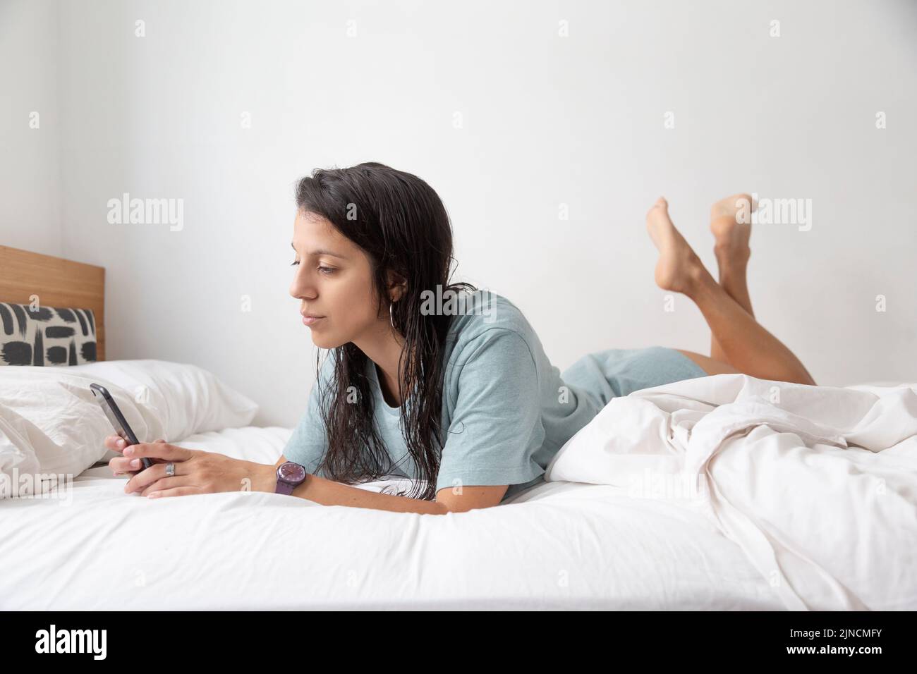 Kaukasische Frau, die auf einem weißen Bett mit Mobiltelefon chattet Stockfoto