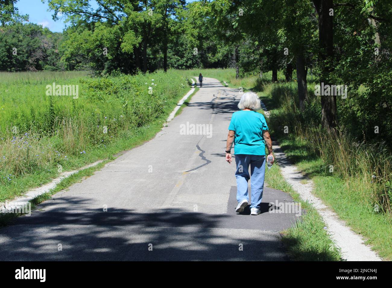 Alte Frau mit langen Haaren, die im Sommer auf dem North Branch Trail in Miami Woods in Morton Grove, Illinois, spazierengeht Stockfoto