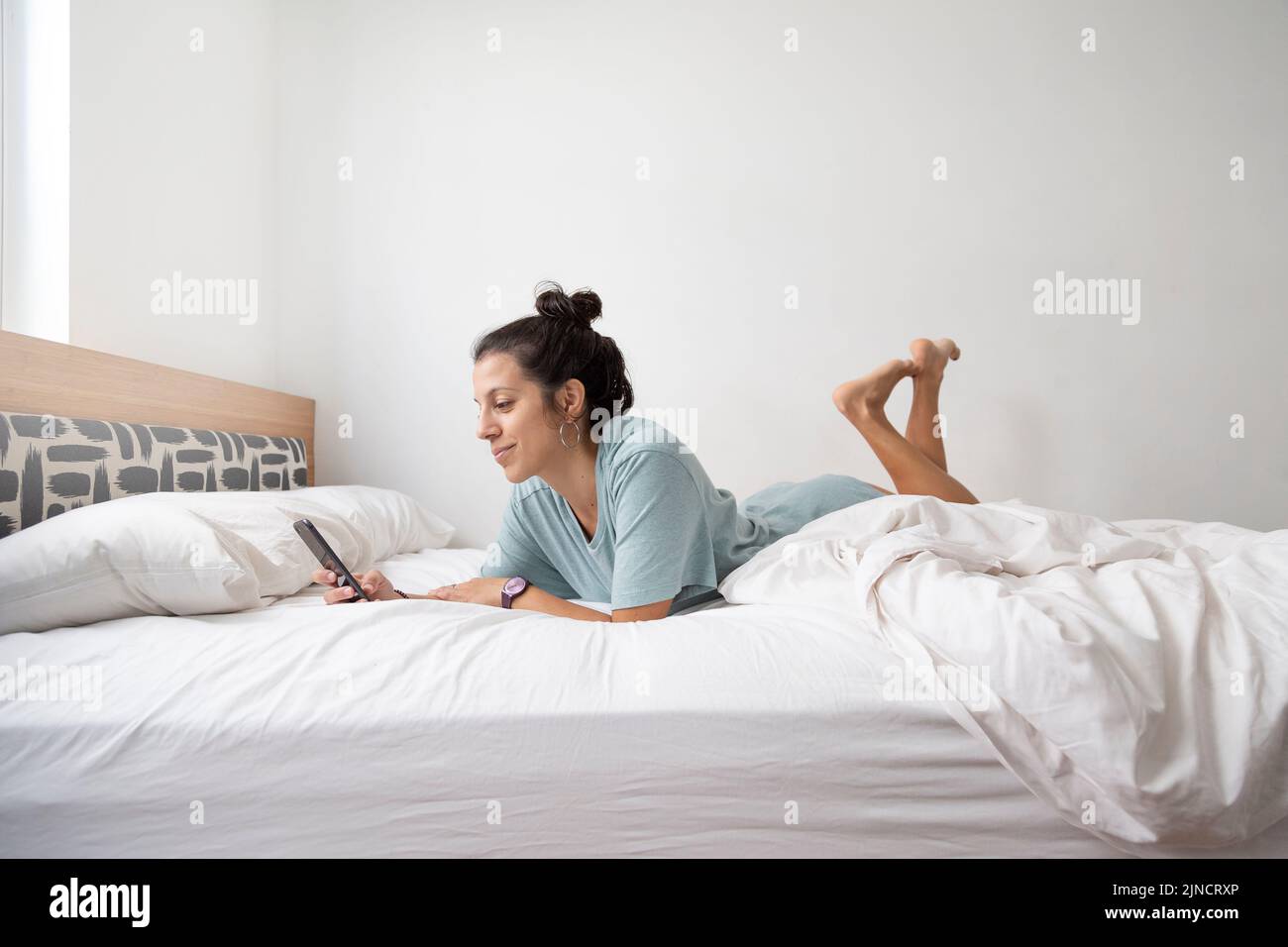 Kaukasische Frau, die auf einem weißen Bett mit Mobiltelefon chattet Stockfoto