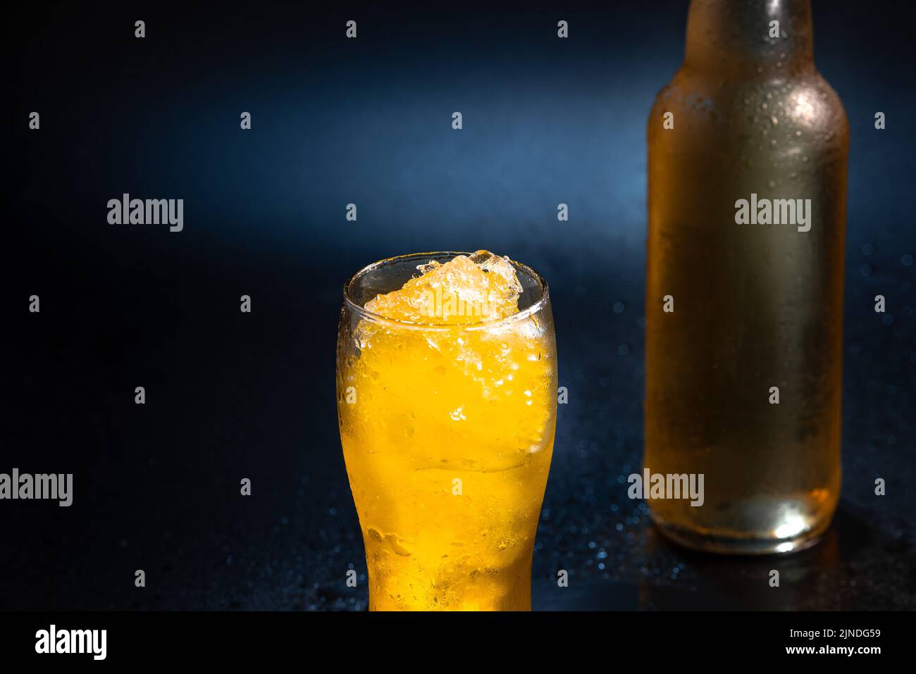 Biercocktail in einem Bierglas auf schwarzem Hintergrund mit Eisstücken neben einer Bierflasche ohne Beschriftung. Ein erfrischender Sommercocktail. Bier Stockfoto