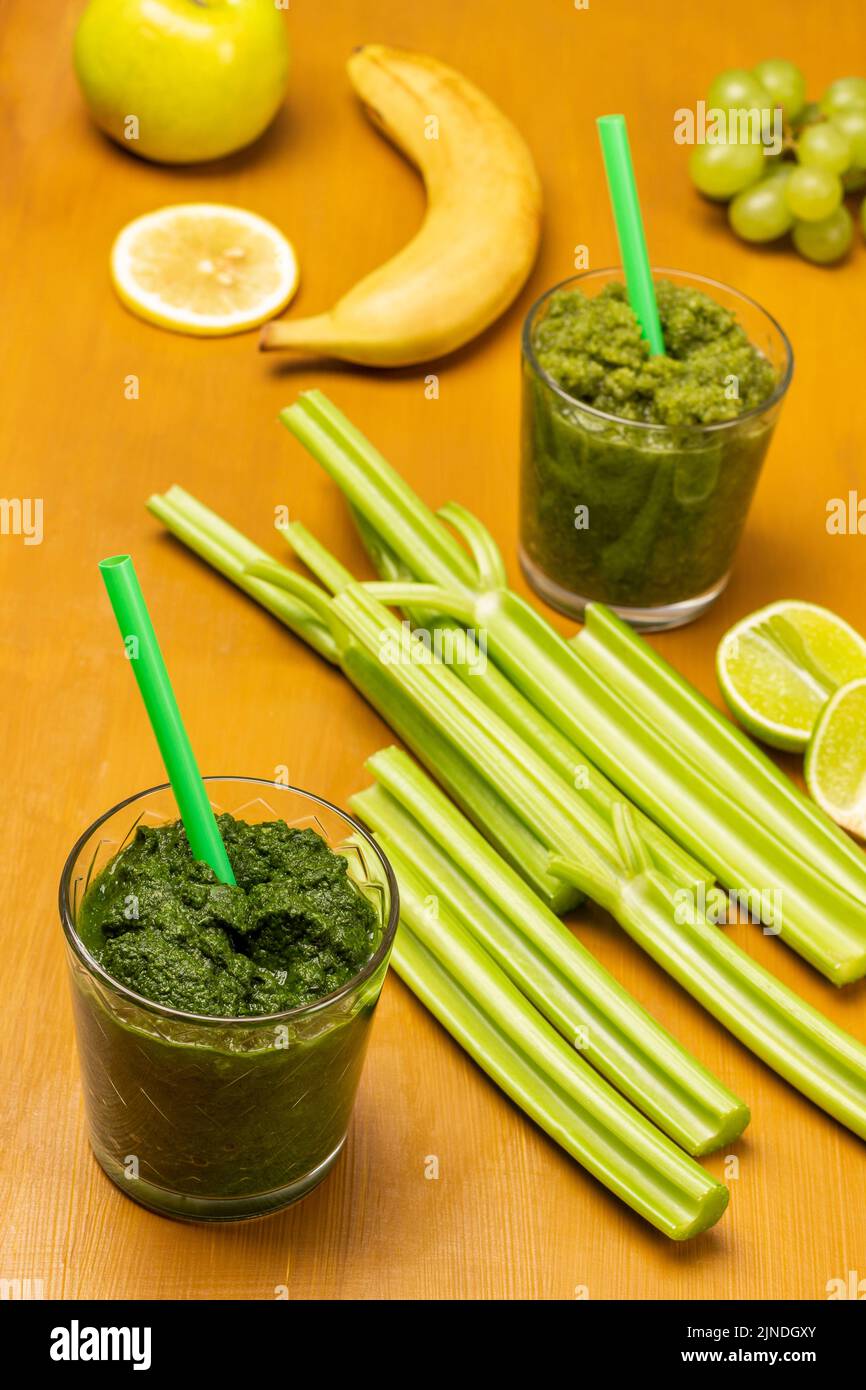 Grüner Smoothie und Stroh in Gläsern. Sellerie-Stängel und Banane auf dem Tisch. Heller Senfhintergrund. Draufsicht Stockfoto
