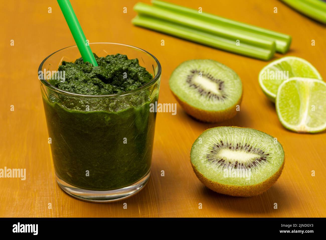 Grüner Smoothie und Stroh im Glas. Kiwi- und Limettenscheiben, Sellerie ...