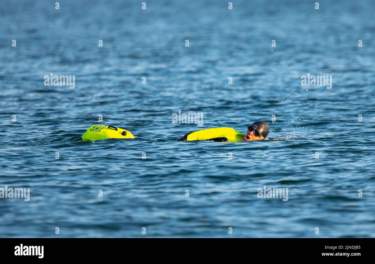 Mann mit Schwimmer und fluoreszierender Kleidung, schwimmt im Meer oder Ozean an einem Sommertag in Großbritannien. Stockfoto