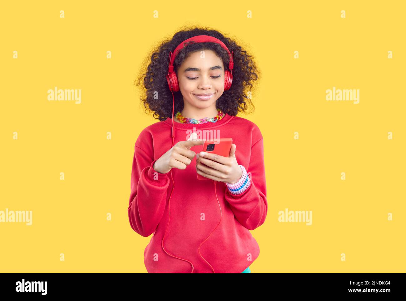 Glückliches Kind in Kopfhörern, das das Mobiltelefon hält, Musik hört oder eine Bildungs-App nutzt Stockfoto