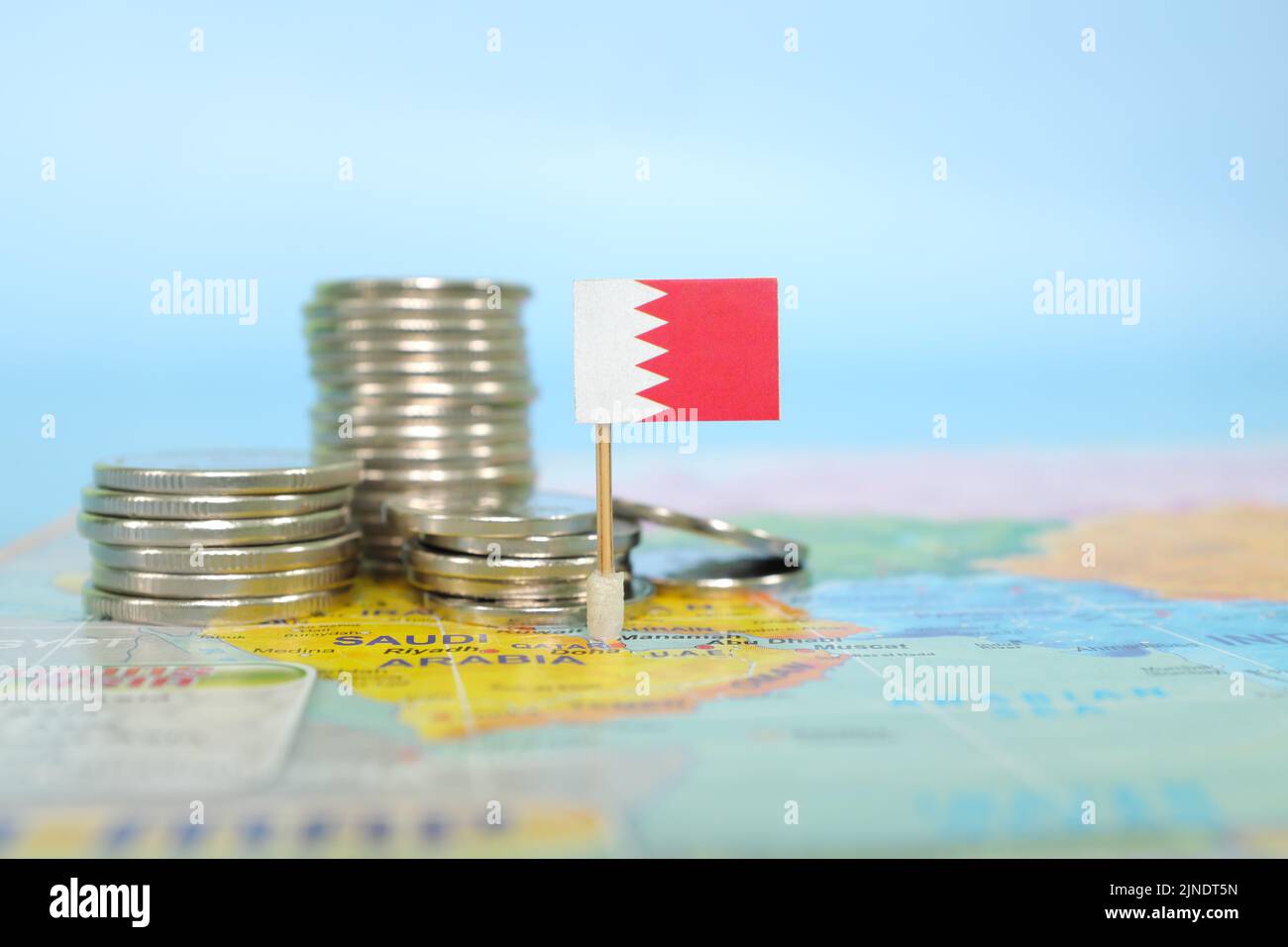 Selektiver Fokus der Bahrain-Flagge auf verschwommener Weltkarte mit Münzen. Bahrains Wirtschafts- und Wohlstandskonzept. Stockfoto