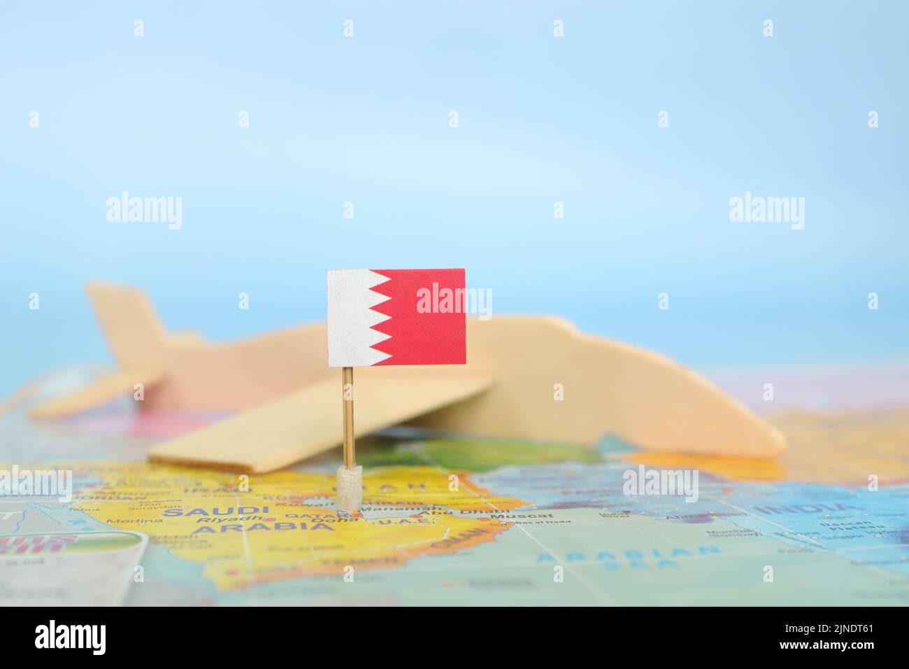 Selektiver Fokus der Bahrain-Flagge auf verschwommener Weltkarte und hölzernen Flugzeugmodellen. Bahrain als Reise- und Tourismusdestinationskonzept. Stockfoto